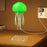 Green jellyfish-shaped lamp on a wooden surface with a wall socket in the background.